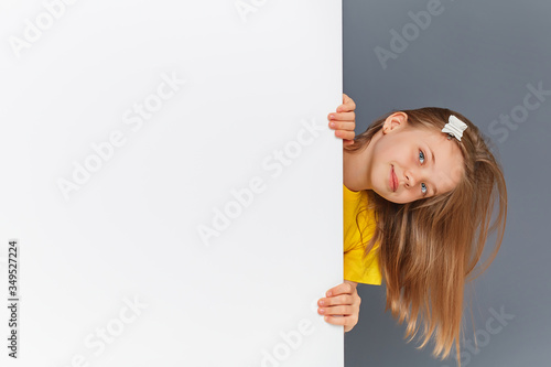 Funny teen girl in yellow clothes looks over a white wall sign.