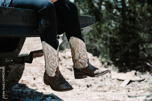 Woman wearing worn brown cowboy boots swings her legs from truck tailgate