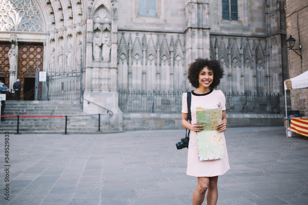 Cheerful ethnic woman with map near ancient stone building