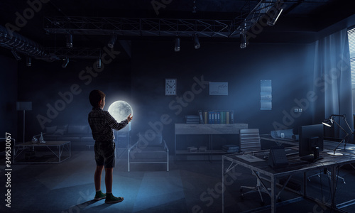 Boy holding moon at night in the office