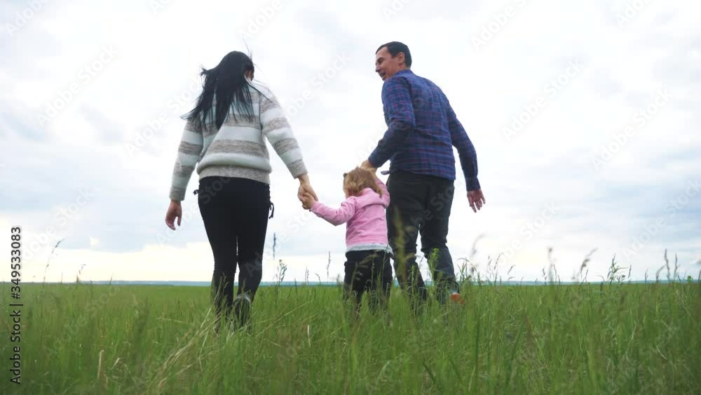 happy family. mom dad and little child a are running in the park raise hands play teamwork outdoors holding hands. woman man and little girl lifestyle raise up hands on green field at sunset happy family. mom dad and little child a are running in the park raise hands play teamwork outdoors holding hands. woman man and little girl lifestyle raise up hands on green field at sunset