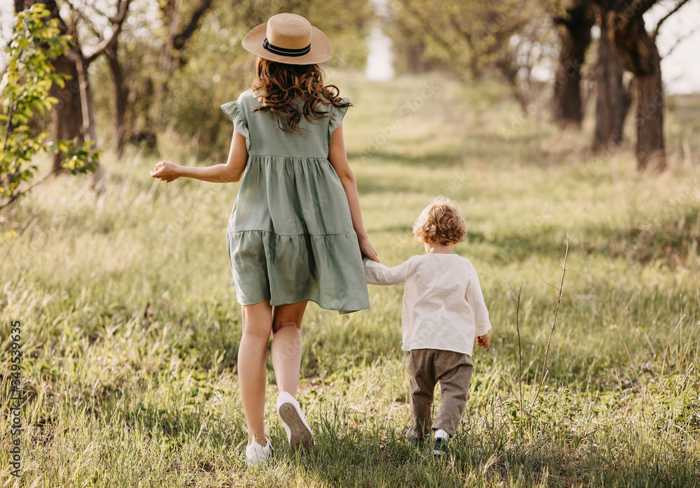 Fototapeta premium Mother and son wearing summer vintage clothes, walking in a park, outdoors, holding hands. Woman and a boy on a summer day.