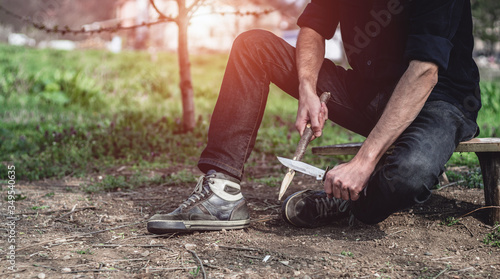 Man sharpening a stake outdoors. Male using a hunting knife and cutting a small branch. Bushcraft, camping and survival concept. photo