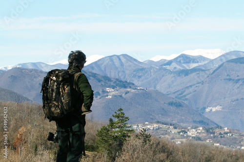 Hiker senior man with backpack and camera standing on the mountain top - Active traveler pensioner with grey hair - Discovery travel destination concept, Motivation - Rear view with copy space