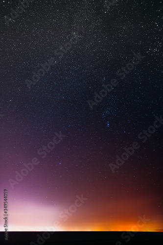 Night Starry Sky With Glowing Stars Above Countryside Landscape. Milky Way Galaxy And Rural Field Meadow In Early Spring. Bright Glowing Stars