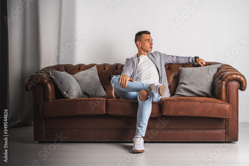 portrait of a young, handsome man sitting pensively on a brown leather sofa 
