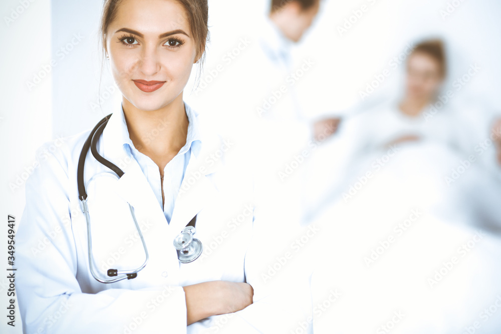 Female doctor smiling on the background with patient in the bed and two doctors Female doctor smiling on the background with patient in the bed and two doctors
