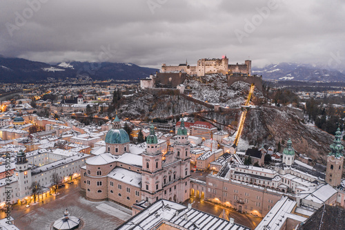 Fototapeta Naklejka Na Ścianę i Meble -  Aerial drone overview of Snow covered Salzburg dome at foot of Hohensalzburg fortress at dusk in in winter time
