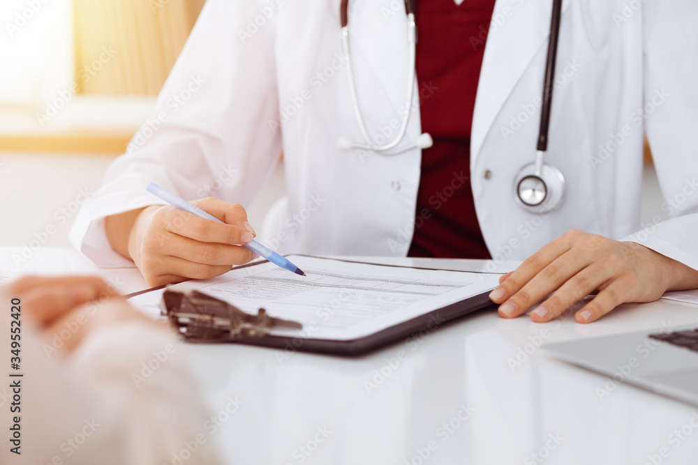 Unknown woman-doctor consulting patient and using clipboard with a medication history record in sunny room. Medicine concept Unknown woman-doctor consulting patient and using clipboard with a medication history record in sunny room. Medicine concept