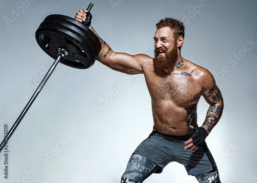 Strong man does landmine exercises, workout with barbell. Photo of sporty man on grey background. Strength and motivation photo