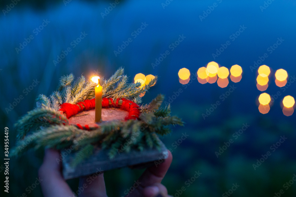 Fototapeta premium A hand holds a wreath and a fire on a Board close-up, a mysterious ancient Slavic pagan ritual, the light of lights on the lake in a blurred background
