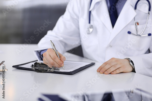 Unknown male doctor sitting and working with clipboard of medication history record in clinic at his working place  close-up. Young physician at work. Perfect medical service  medicine concept
