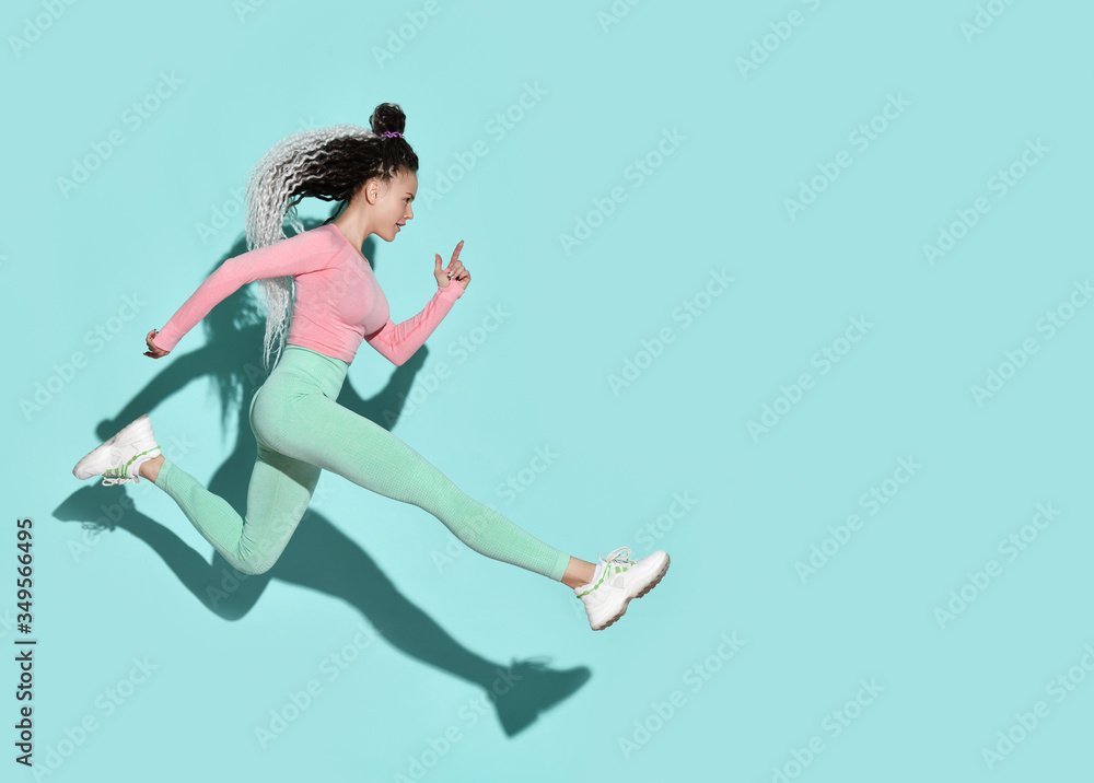 Young beautiful smiling girl with modern hairstyle in sportswear and sneakers jumping running with legs stretched out