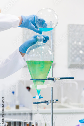 Hand operating with blue liquid in separatory funnel photo