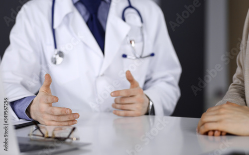Unknown male doctor and patient woman discussing something while sitting in clinic and using clipboard. Best medical service in hospital, medicine, pandemic stop