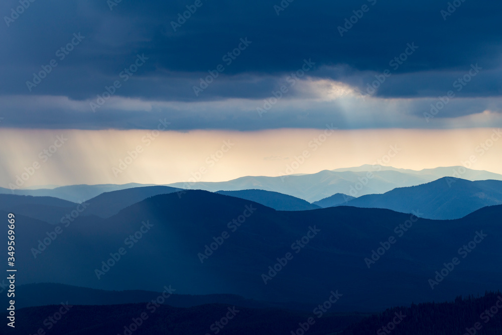 Rain over the mountains against the backdrop of foggy mountain ranges and a cloudy sky. View of the rain clouds over the wooded mountains. Carpathian, Ukraine, Europe