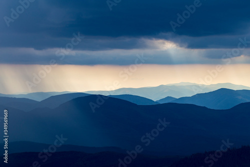 Rain over the mountains against the backdrop of foggy mountain ranges and a cloudy sky. View of the rain clouds over the wooded mountains. Carpathian, Ukraine, Europe