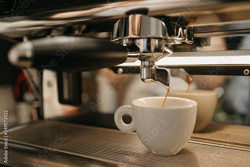 Espresso brewing in a professional espresso machine in a coffee shop. A close-up of a coffee pouring in a white cup from a coffee machine in a cafe.