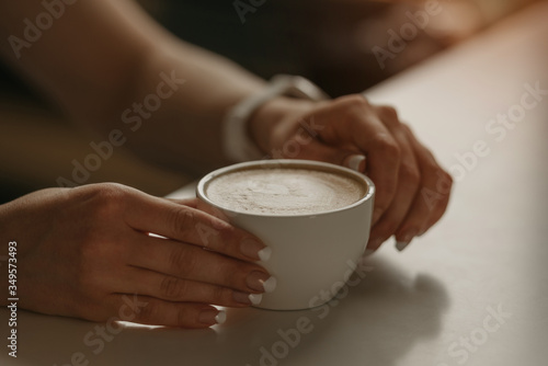 A girl with beautiful nails keeps a cup of latte in her hands in a cafe. 