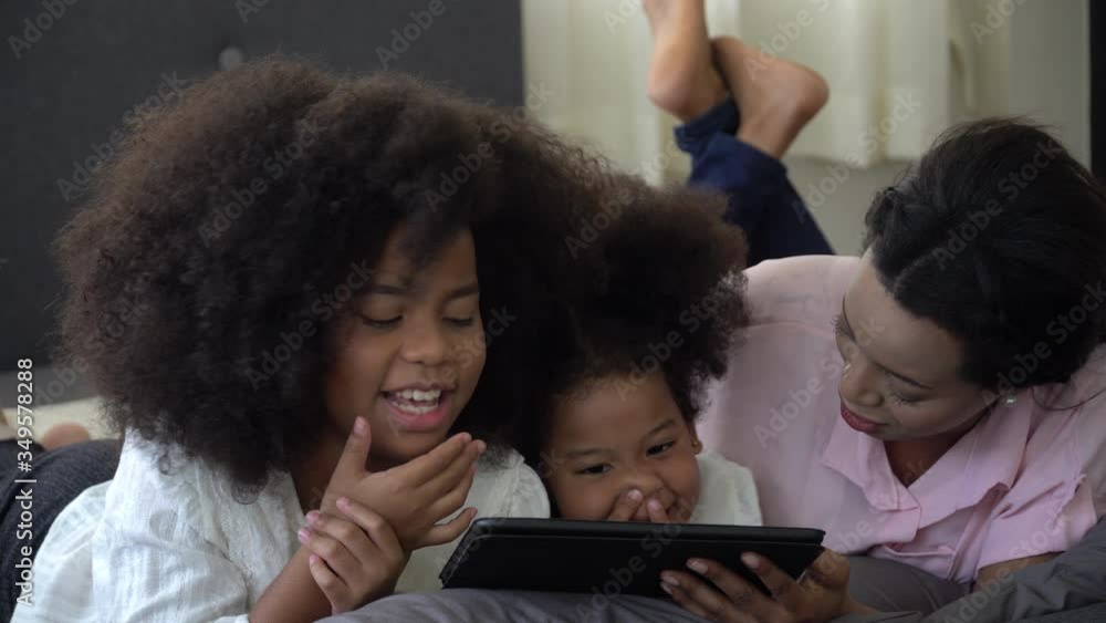 african american single mom with two daughter lying down on bed looking tablet computer together having fun stay at home . Happy black family with internet techmology . african american single mom with two daughter lying down on bed looking tablet computer together having fun stay at home . Happy black family with internet techmology .