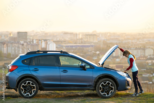 Fotografie Young woman opening bonnet of broken down car having trouble with her vehicle