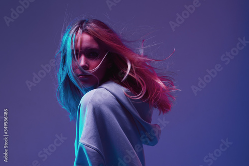 Portrait of a stylish young girl, cool posing in a hoodie with developing hair, on a neon background.