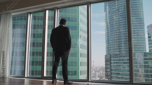 Young successful businessman standing in front of the windows, looking into the distance to the city. Successful man stands in the neoboksreb. A businessman stands in front of a window.