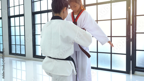 Trainer helping girl to adjust training costume for taekwondo