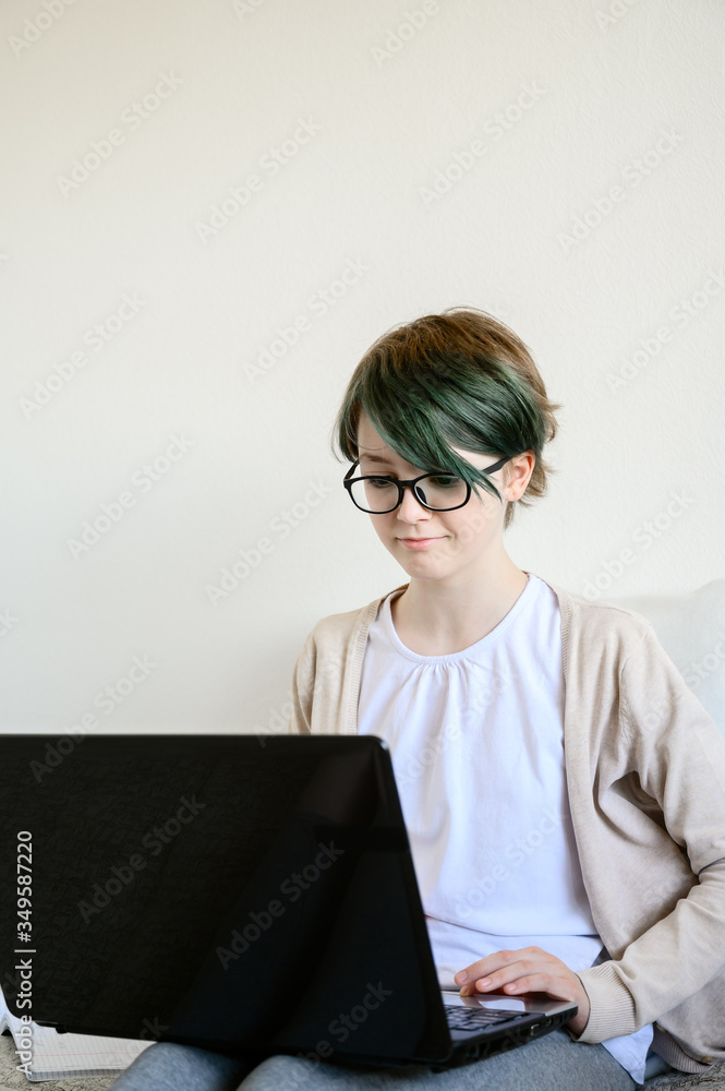 Distance learning online education. Teen schoolgirl studying at home, using laptop. Caucasian girl with glasses sitting on bed and doing school homework. Copy space, vertical shot. Distance learning online education. Teen schoolgirl studying at home, using laptop. Caucasian girl with glasses sitting on bed and doing school homework. Copy space, vertical shot.