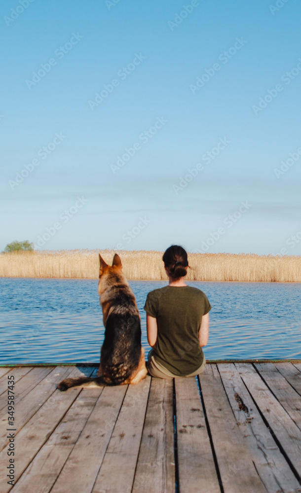 A girl and a German shepherd sit by the river. Girl with a dog in nature by the lake.