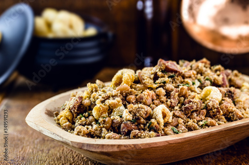 "Feijão tropeiro", typical Brazilian food, in a wooden bowl with rustic cuisine, with rustic cuisine in the background. Food from minas gerais.