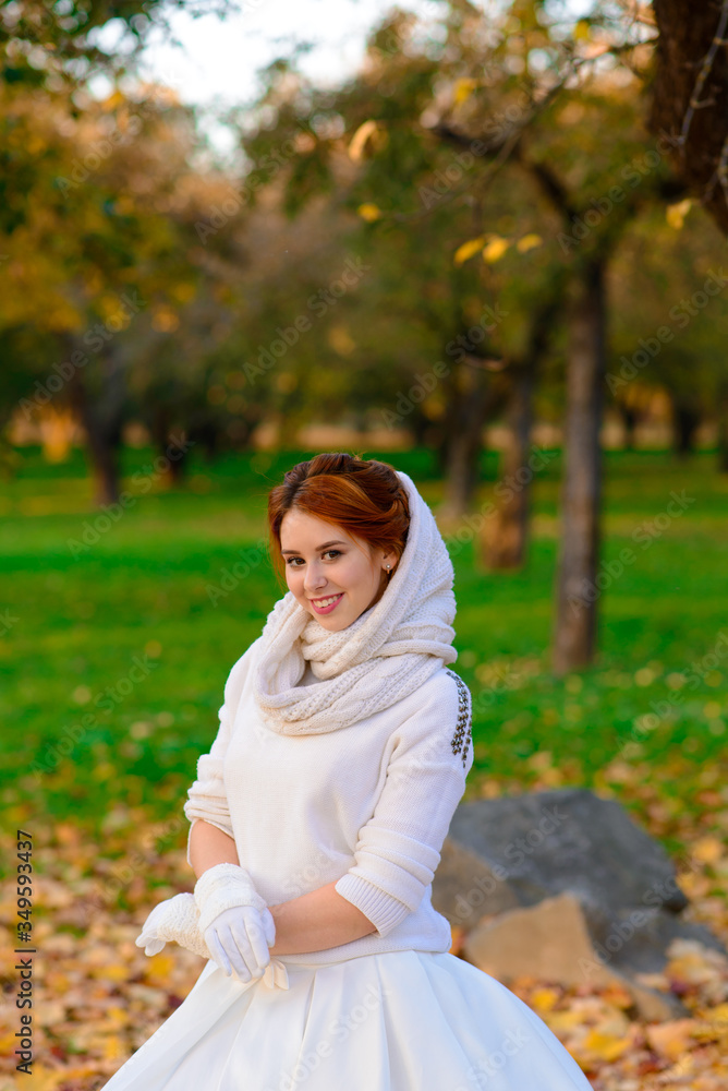 Portrait of a beautiful young redhead girl with flowers look attractive in a white dress on a background of autumn forest and leaves posing and smiling. Portrait of a beautiful young redhead girl with flowers look attractive in a white dress on a background of autumn forest and leaves posing and smiling.