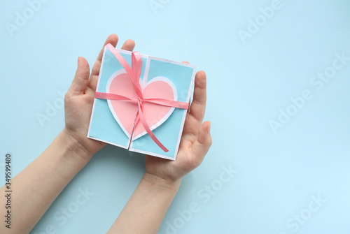 Greeting card with a pink heart and a pink ribbon tied on a bow in the hands of a Caucasian man on a blue background. Space for text. Copy space. Greeting card for Valentine's day and mother's day.