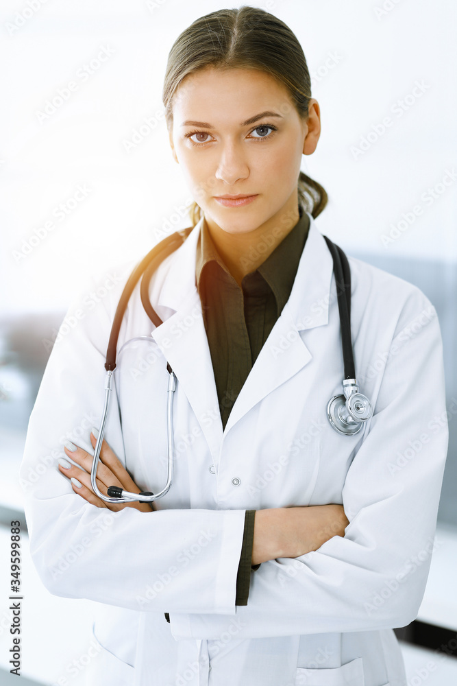 Woman-doctor standing and looking at camera in sunny clinic. Perfect medical service. Medicine and healthcare