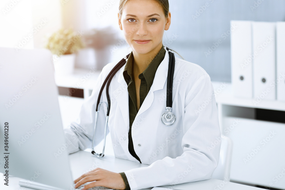 Woman-doctor typing on pc computer while sitting at the desk in sunny hospital office. Data in medicine and healthcare Woman-doctor typing on pc computer while sitting at the desk in sunny hospital office. Data in medicine and healthcare