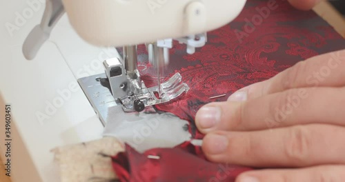 Handsome Male hand pushes red paisley lining material through a sewing machine during suit making process. Fashion, creation and tailoring. High angle view