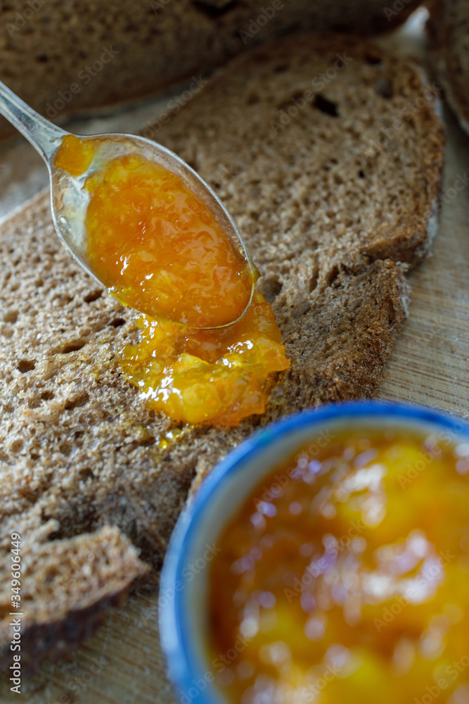 Serving a spoonful of orange jam on a slice of rye bread. Kumquat jam.