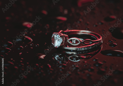 Gold rings with a diamond in blue-red neon light on a dark background with drops of water