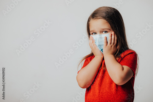 Little european girl wearing mask for protect pm2.5 and Covid-19. Sick child Little girls look at the camera posing in the studio in a red dress with a medical mask on her face. Copy space. 