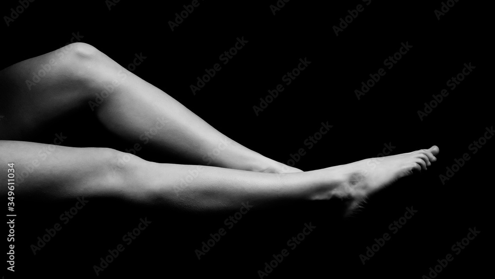Fototapeta premium black and white photo of female legs lying on a black void and pulling toes, side view isolated on black background