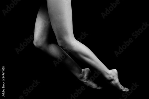 black and white photo of female legs standing on bent fingertips isolated on black background