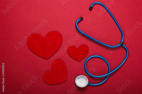 Stethoscope with hearts on red background. Top view