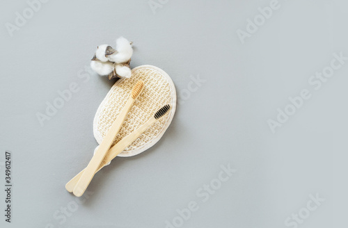Two bamboo brushes for brushing teeth, lie on a bamboo brush for the face, and a cato flower on a gray background. Place for text