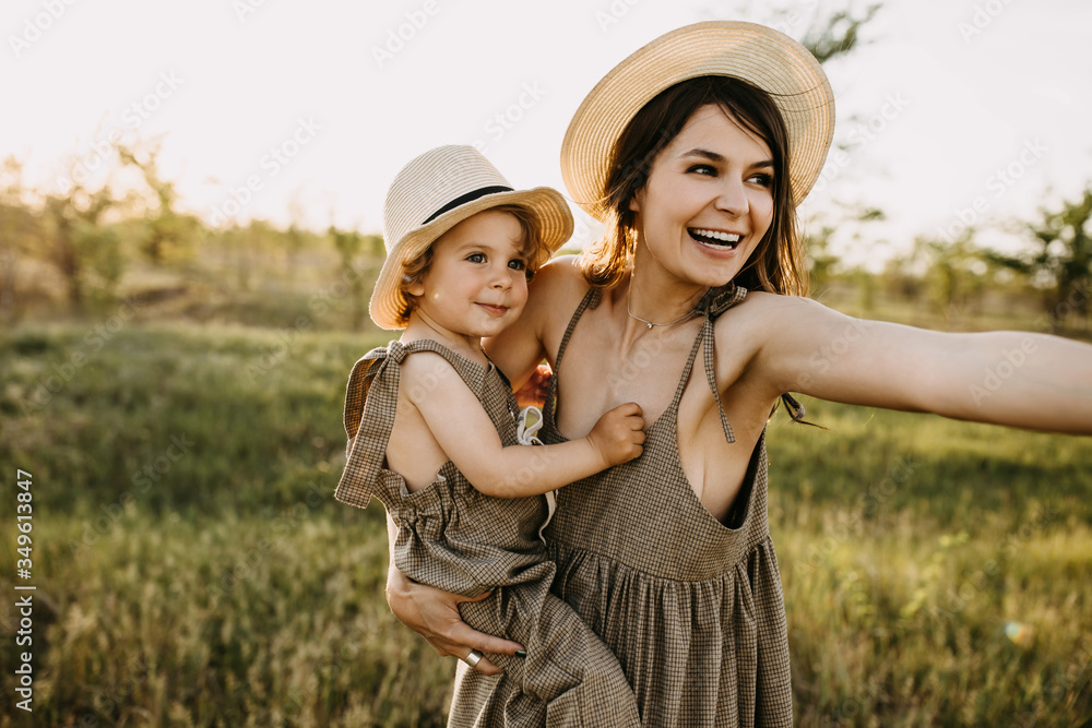 Young woman and little boy in a field, outdoors. Mother holding her son, smiling, both wearing vintage clothes and straw hats.