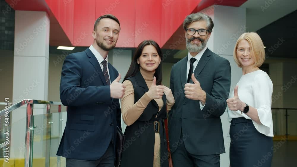 Portrait of happy business people male and female showing thumbs-up hand gesture and smiling standing in office building hall. Team and success concept. Portrait of happy business people male and female showing thumbs-up hand gesture and smiling standing in office building hall. Team and success concept.
