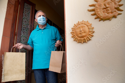 Anziano con mascherina e Polo azzurra è fermo sull'uscio di casa con le buste della spesa photo