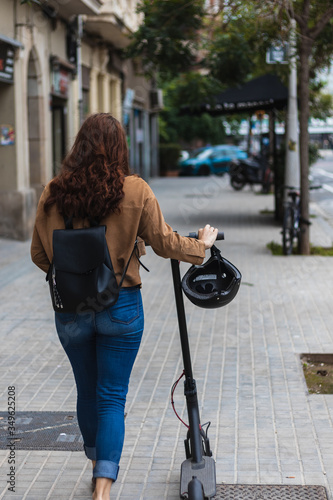 Unrecognizable woman in casual clothes pushing electric scooter