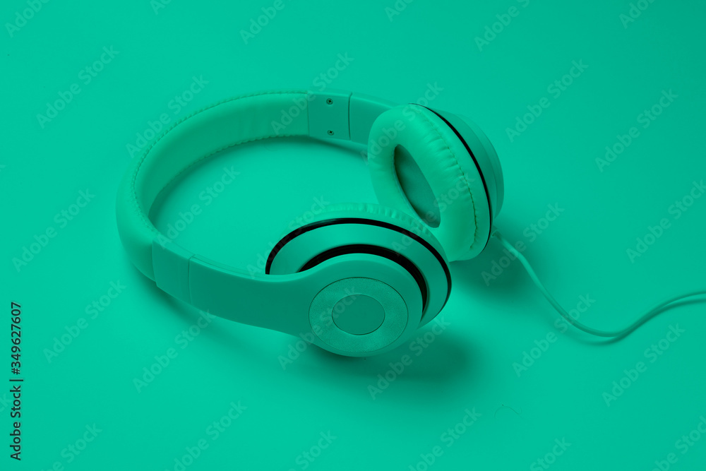 Classic white wired headphones in green neon light. Retro style. 80s. Pop culture. Top view. Minimal Music Concept Classic white wired headphones in green neon light. Retro style. 80s. Pop culture. Top view. Minimal Music Concept