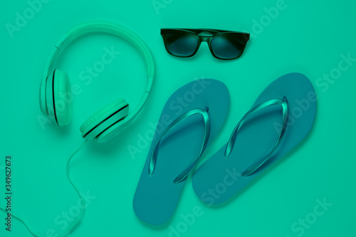 Accessories for relaxing on the beach. Flip flops, headphones, sunglasses. Studio shot in green neon light. Top view
