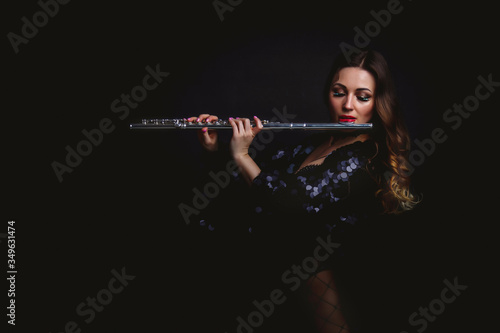 Female girl artist in suit with flute on black background. Flute in hand. Player with orchestra instrument. Isolated on black. The concept of music poster